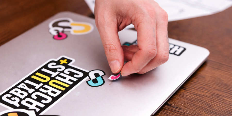 Hand placing a colorful sticker on a laptop with a wooden surface underneath