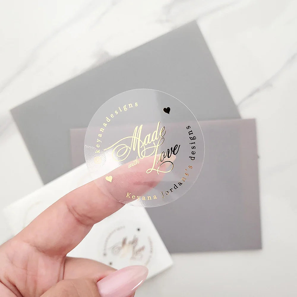 Transparent round gold foil logo sticker held in hand for luxury packaging